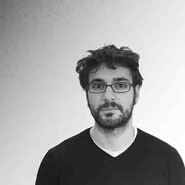 Headshot of David Petrevski, Design Technology Specialist, smiling in a textured leather jacket, white shirt, and tie, presented in black and white against a blurred background.